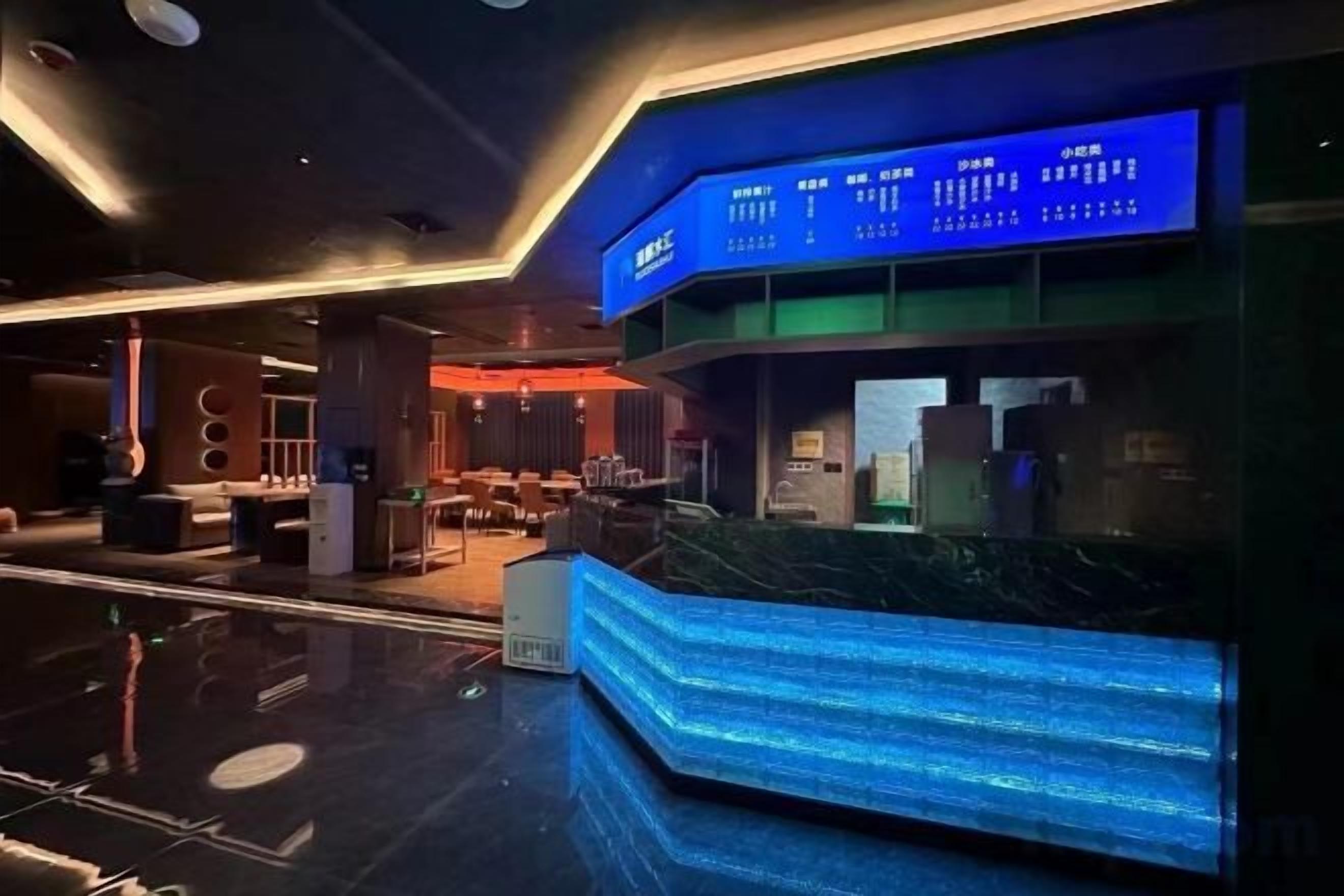 A modern hotel lobby with a reception desk, seating area, and a digital display board.