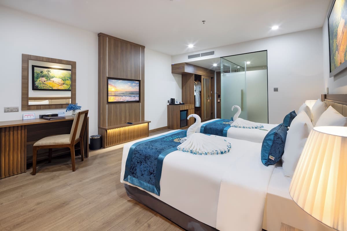 Ein modernes Hotelzimmer mit einem großen Bett, einem Schreibtisch und einem Sessel. Ein Fernseher ist an der Wand befestigt und über dem Bett befindet sich ein Spiegel.
