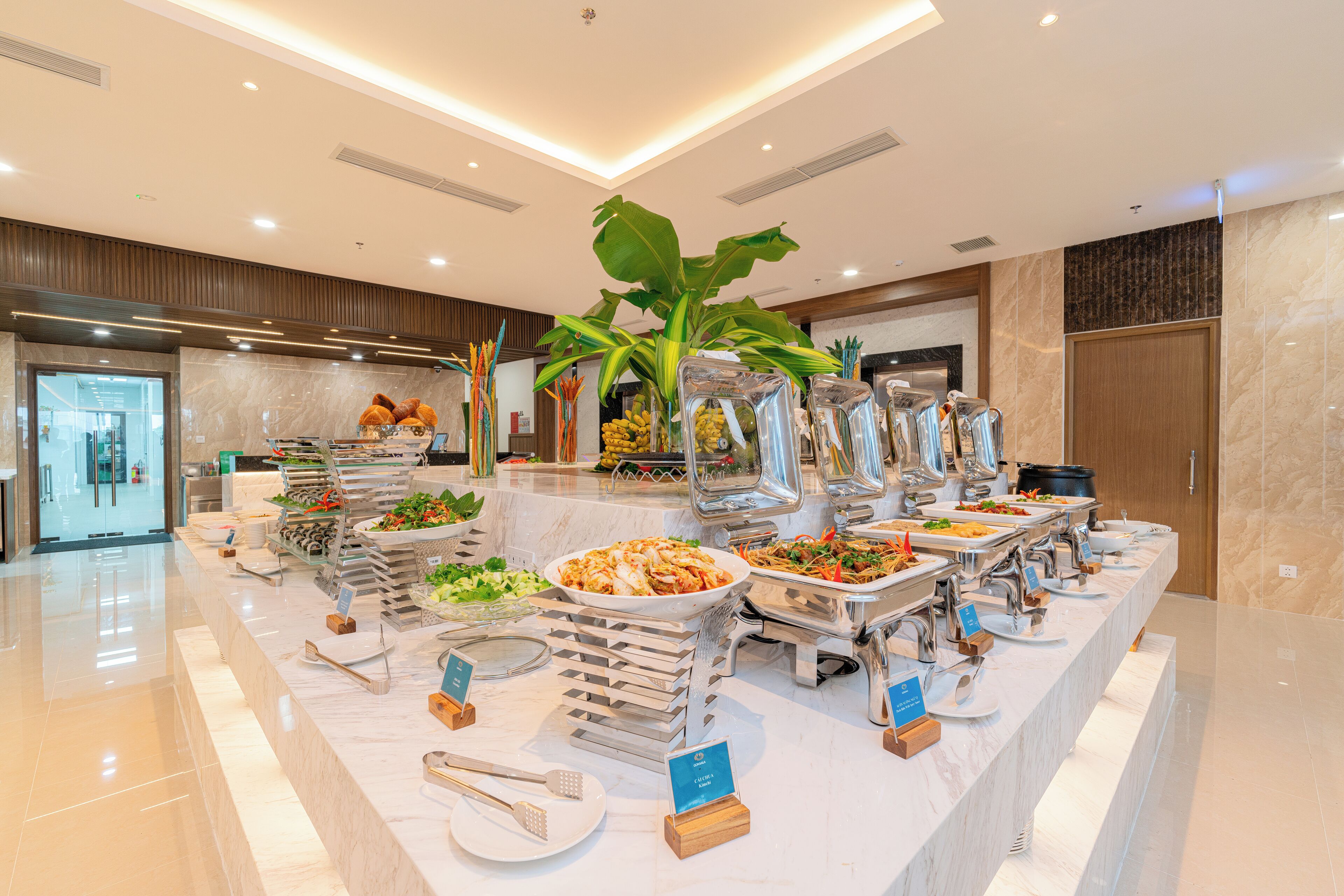 A buffet with various food stations, a large potted plant, and a modern interior design.