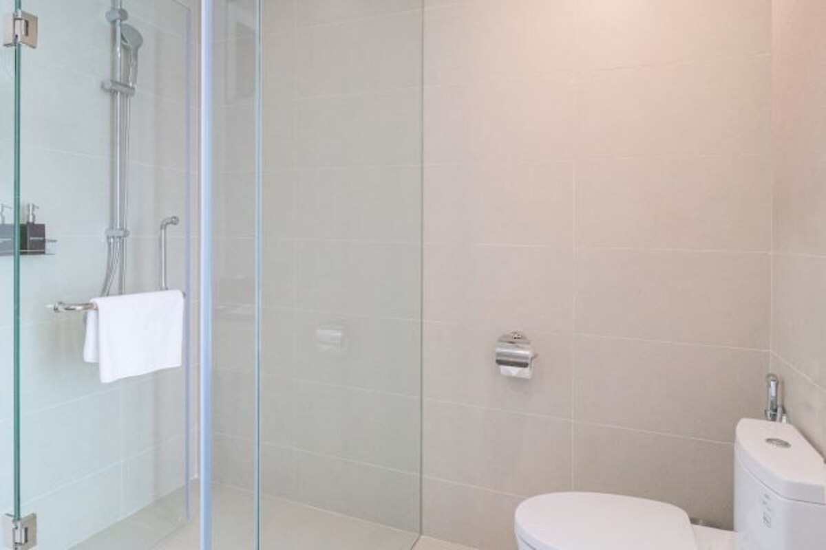 Une salle de bain moderne avec une douche à parois de verre, des toilettes blanches et un porte-serviettes.