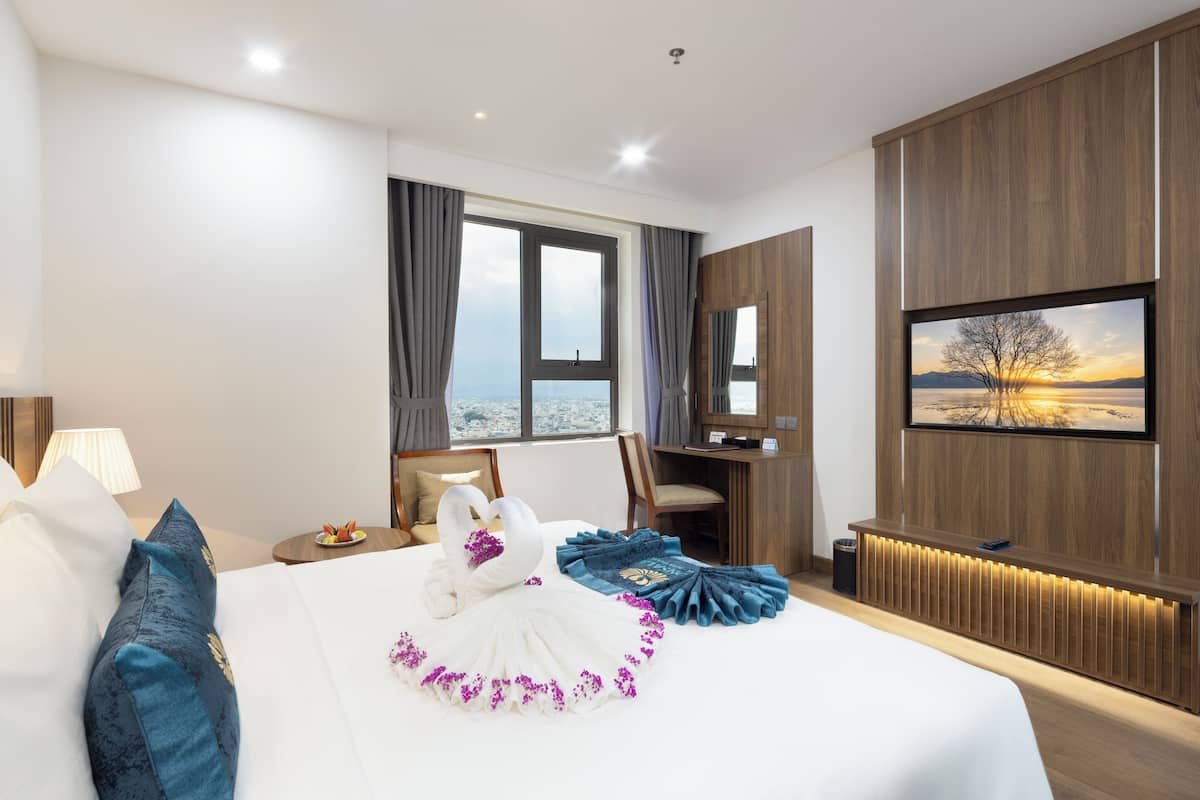 Ein Hotelzimmer mit einem großen Bett, einem Schreibtisch, einem Fernseher und Blick auf die Stadt.