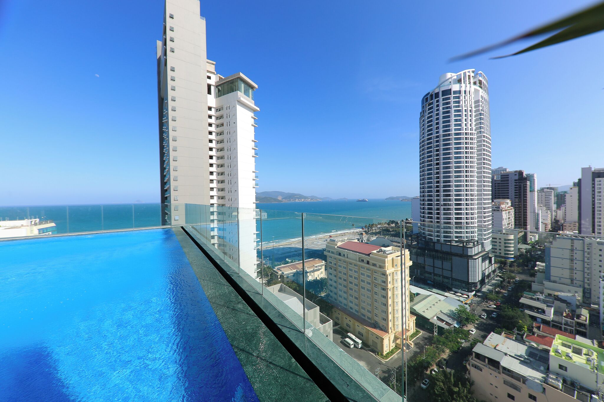 A high-rise building with a pool overlooking a cityscape and the ocean.