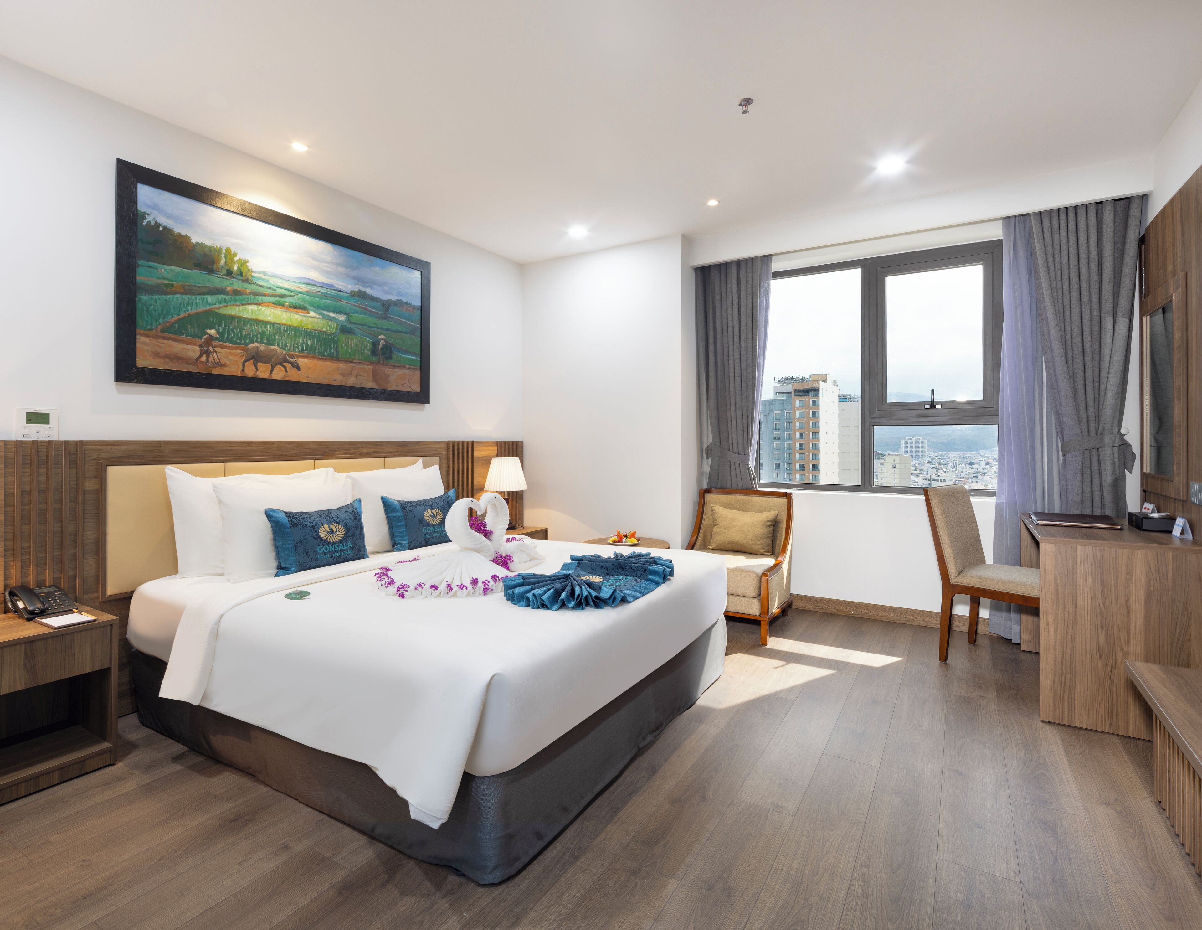 Hotelkamer met een groot bed, een bureau, een stoel, een raam met uitzicht op de stad en een schilderij aan de muur.
