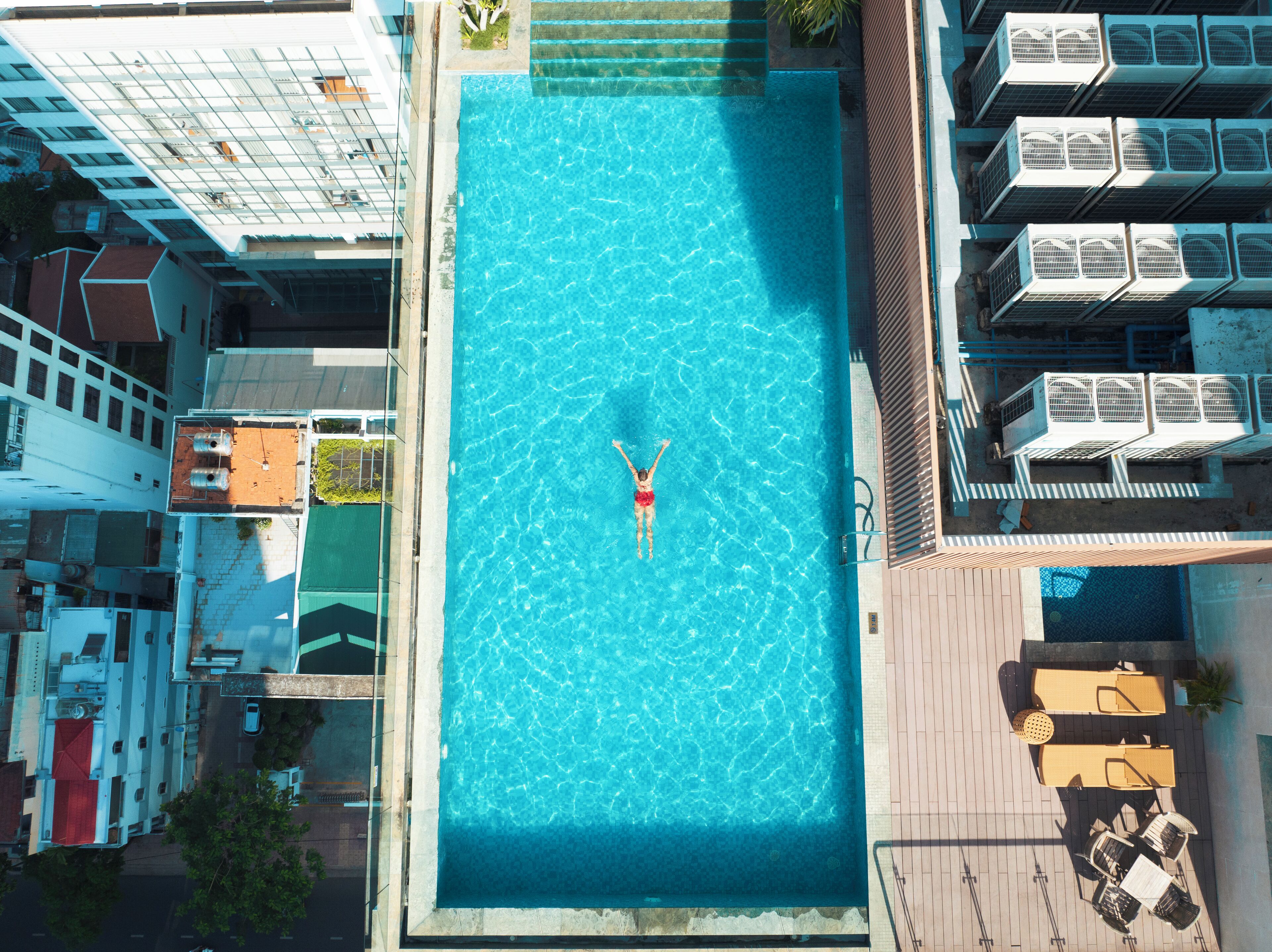 An aerial view of a swimming pool with a person in the center, surrounded by buildings and outdoor seating.