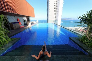 Zona de piscina con vista al mar, un edificio alto y un puesto de socorrista.