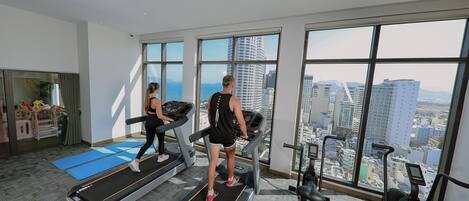 A gym with treadmills and exercise equipment, large windows with a city view, and a yoga mat area.
