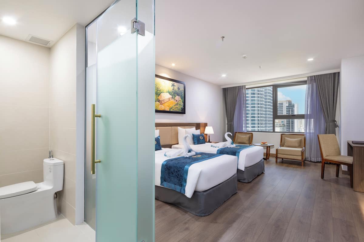 Ein Hotelzimmer mit zwei Betten, einer Sitzecke, einem Badezimmer und einem großen Fenster mit Blick auf die Stadt.
