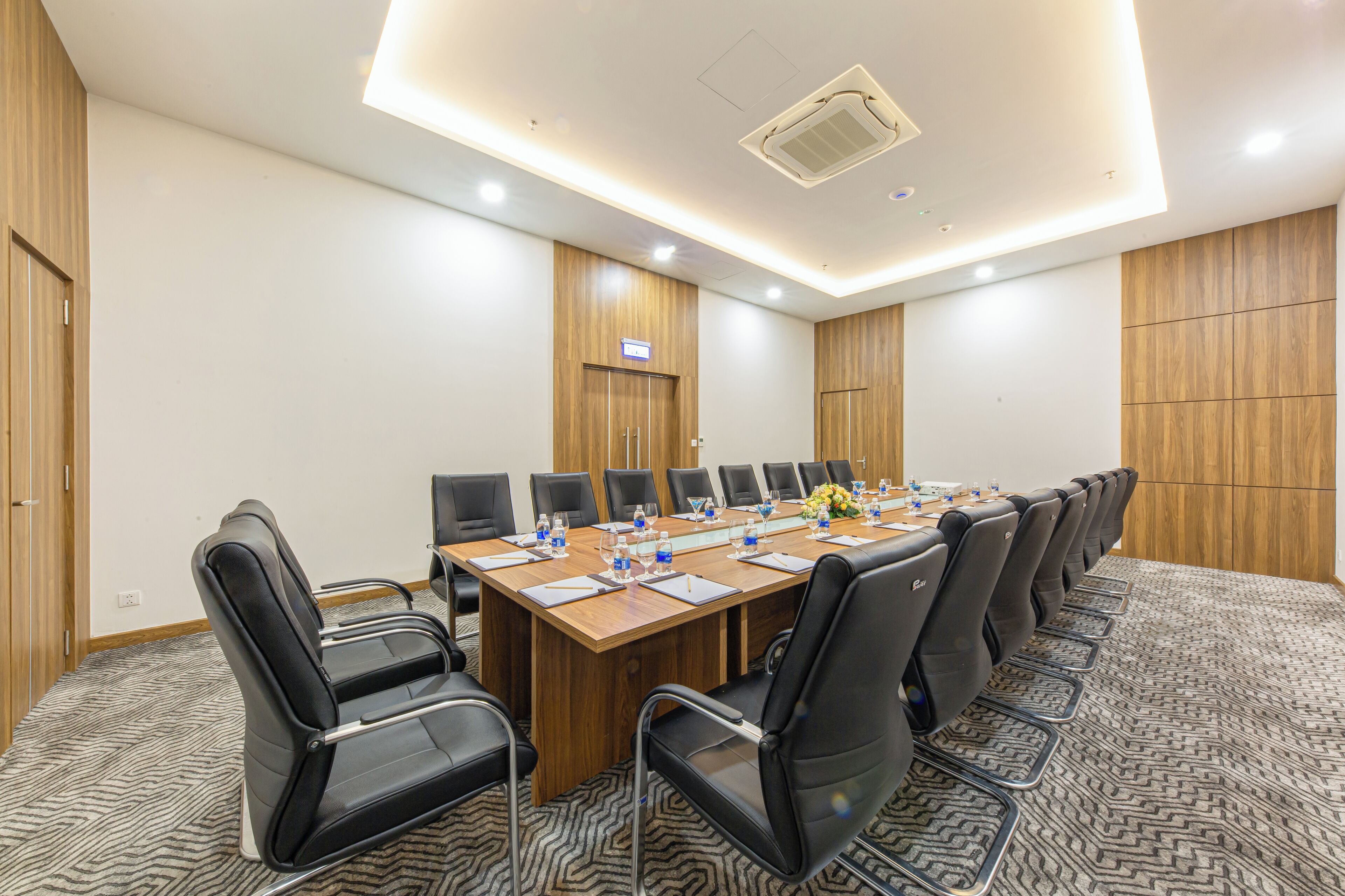 A conference room with a long table, black chairs, and a wooden panel wall.