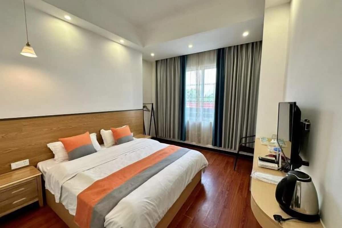 A modern hotel room with a large bed, a bedside table, a flat-screen TV, and a window with curtains.
