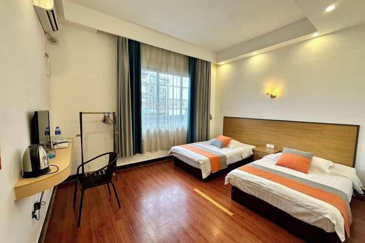 A hotel room with two beds, a desk with a chair, a TV, and a window with curtains.