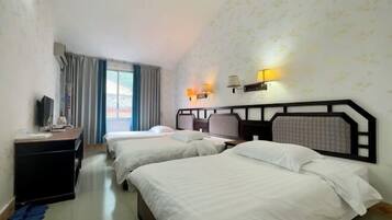 A hotel room with two beds, a desk with a TV, a lamp, and a window with curtains.