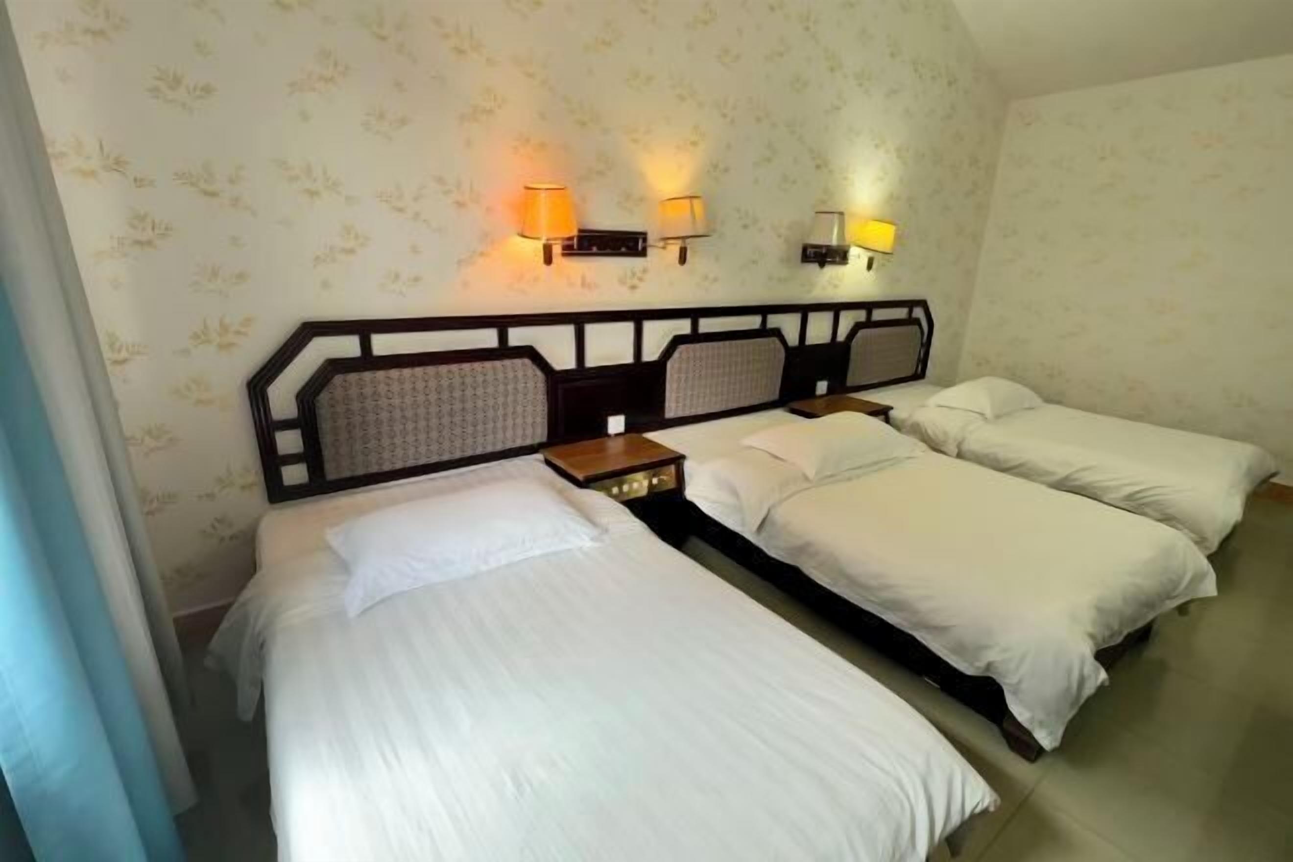 Een hotelkamer met drie eenpersoonsbedden, een nachtkastje en twee wandlampen.