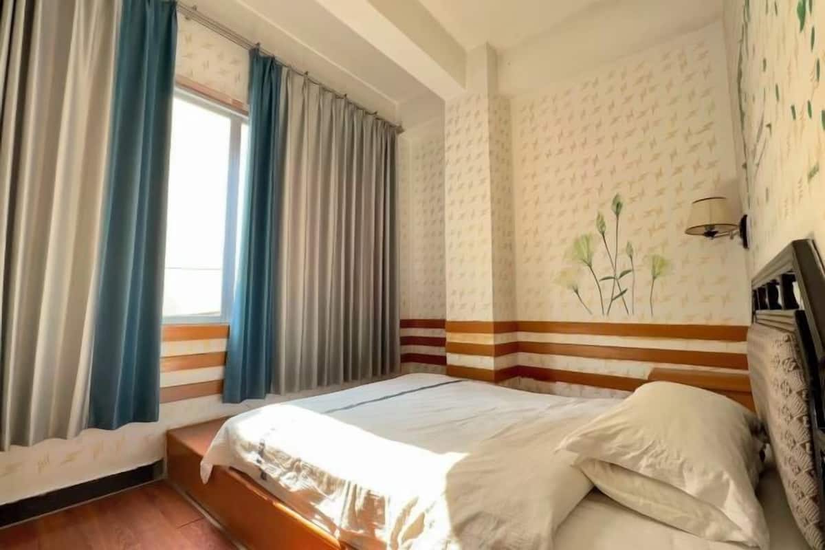 A hotel room with a bed, curtains, a wall with a patterned design, and a wall-mounted lamp.