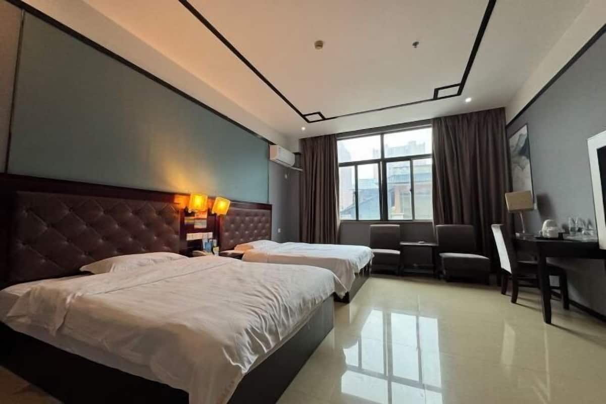 Quarto de hotel com duas camas, uma escrivaninha, uma cadeira e janela com vista para a cidade.