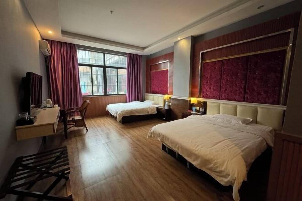 Quarto de hotel com duas camas, uma mesa, uma cadeira e uma janela com cortinas.