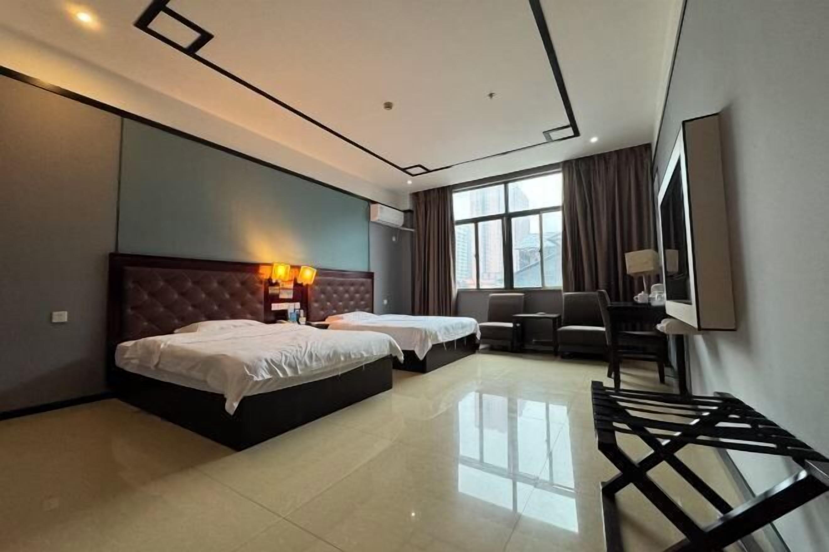 A hotel room with two beds, a desk, a chair, a TV, and a large window with curtains.