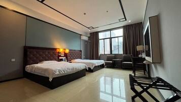 A hotel room with two beds, a desk, a chair, a TV, and a large window with curtains.