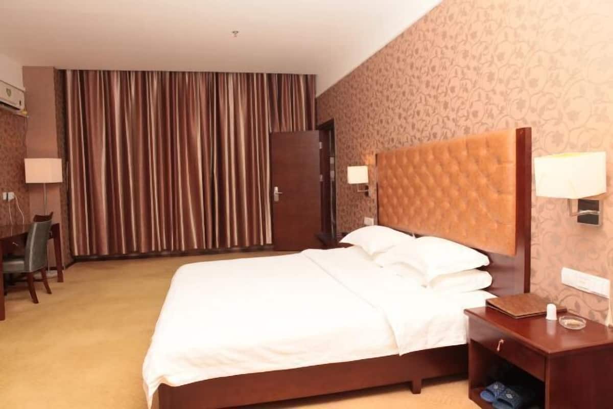 Quarto de hotel com cama, escrivaninha, cadeira, guarda-roupa e cortina.