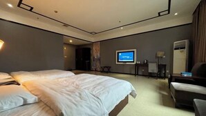 Een hotelkamer met een groot bed, een bureau, een stoel, een televisie en een airconditioner.