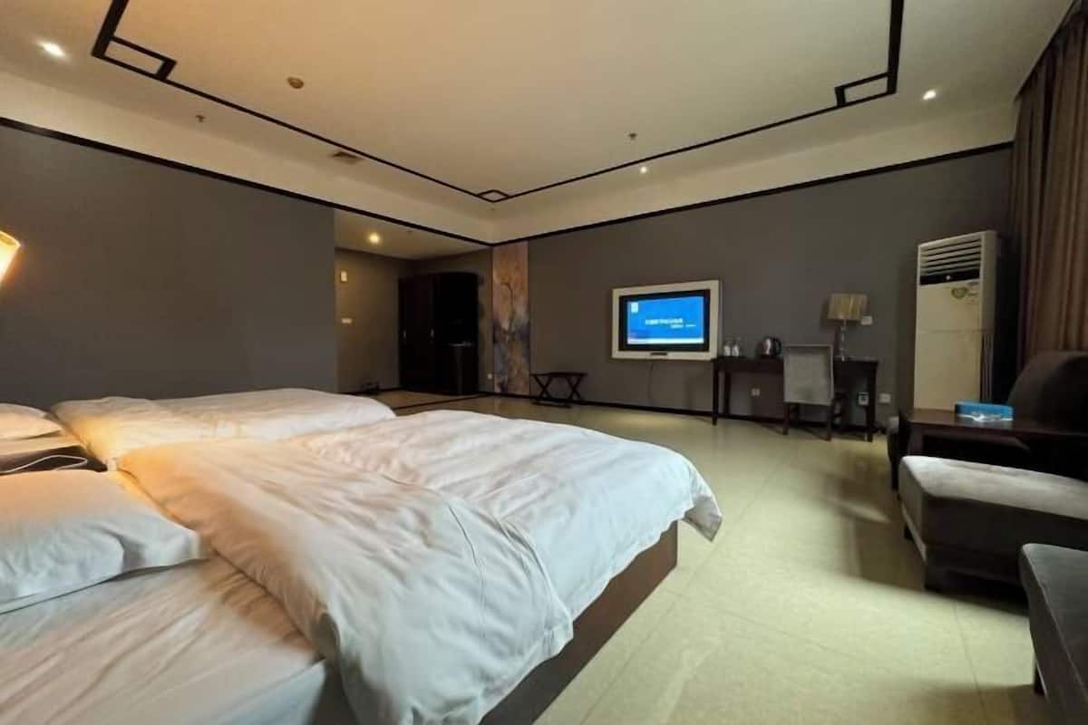 Quarto de hotel com cama grande, escrivaninha, cadeira, televisão e ar condicionado.