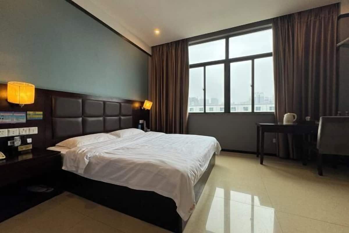 Quarto de hotel com uma cama grande, uma mesa de trabalho e vista da cidade através de uma janela ampla.