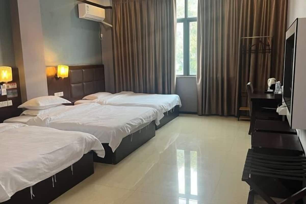Quarto de hotel com três camas, televisão de tela plana, escrivaninha e janela com cortinas.
