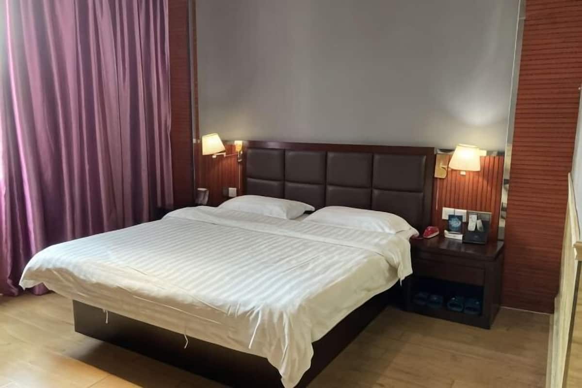 Quarto de hotel com uma cama grande, duas mesas de cabeceira com luminárias, uma cabeceira de madeira e piso de madeira.