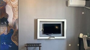 Een kamer met een tv aan de muur, een bankje en een muur met een muurschildering.