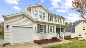 Ein zweigeschossiges Haus mit Veranda, Garage und gepflegtem Rasen.