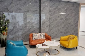 A lobby with a marble wall, a blue chair, a brown sofa with patterned cushions, a yellow armchair, and a small round table with a white top. - New Beacon Shennongjia Villa (Shennongjia)