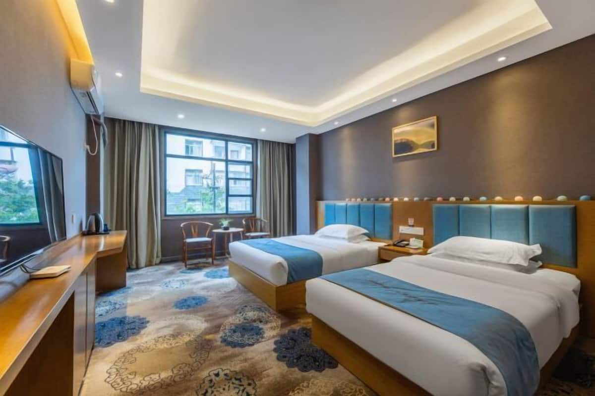 A hotel room with two beds, a desk, a chair, and a large window.