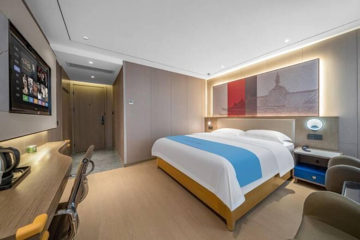 A modern hotel room with a bed, bedside table, chair, and a wall-mounted TV.