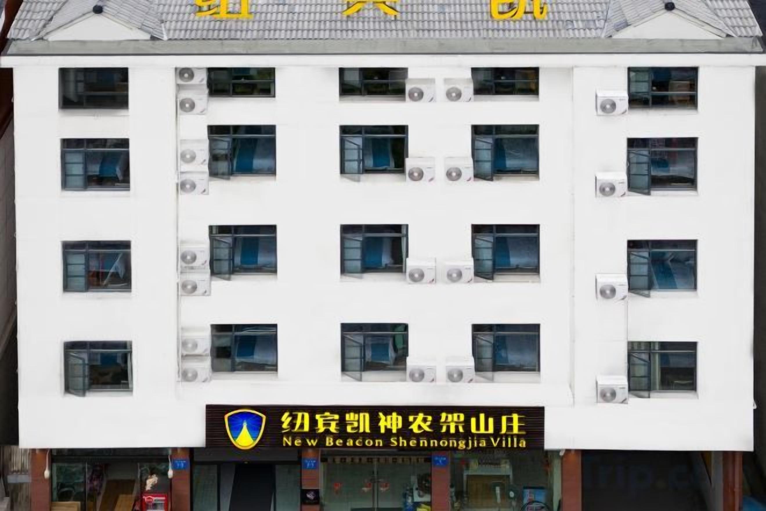 A multi-story building with a white facade, multiple air conditioning units, and a sign indicating it is the New Beacon Shennongjia Villa.