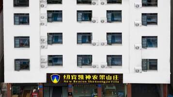 A multi-story building with a white facade, multiple air conditioning units, and a sign indicating it is the New Beacon Shennongjia Villa.