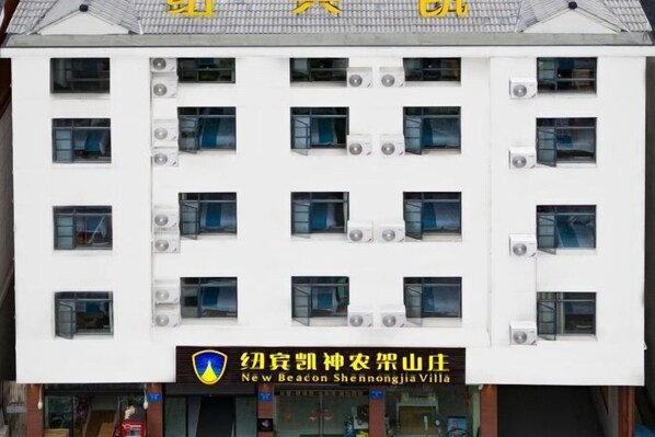 Un immeuble à plusieurs étages, doté d’une façade blanche et de plusieurs unités de climatisation. L’immeuble porte une enseigne avec des caractères chinois et du texte en anglais indiquant qu’il s’agit d’un hôtel.