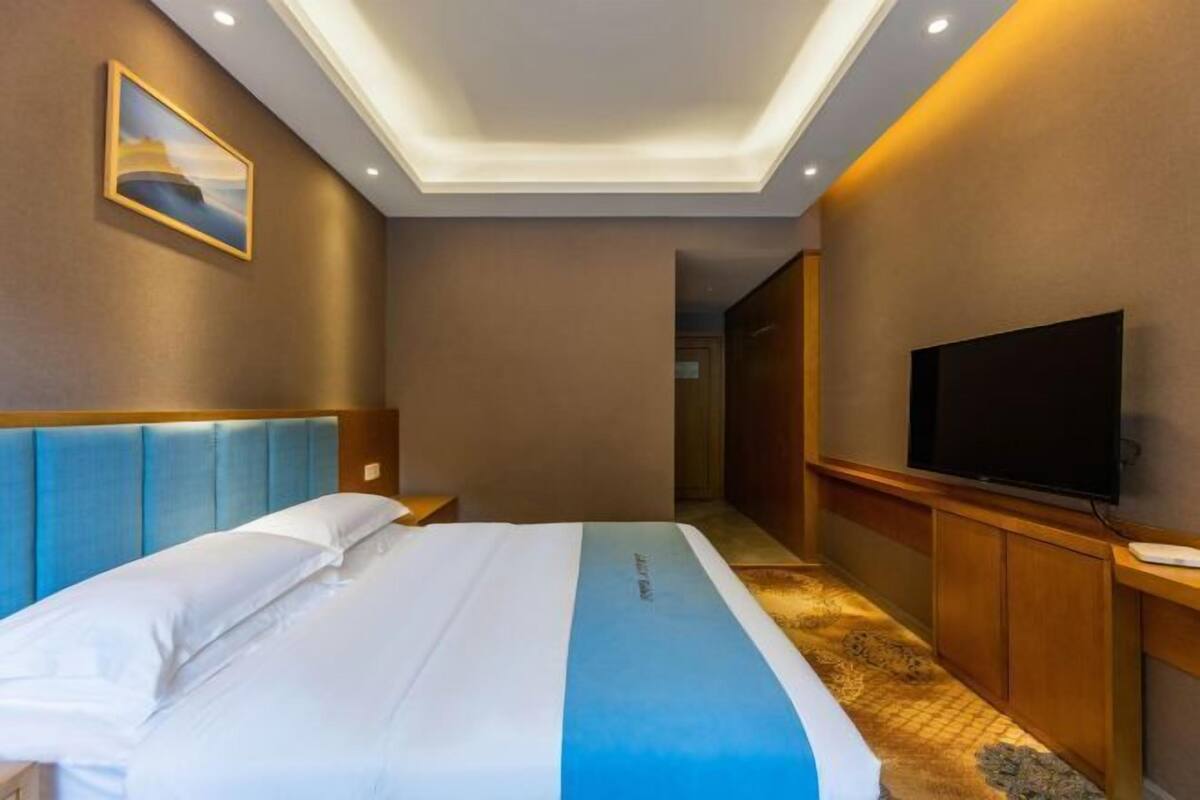 A hotel room with a bed, a television, and a painting on the wall.