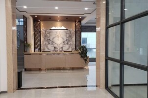 Un área de recepción con mostrador de mármol, una fuente decorativa y una escalera que conduce a un nivel superior.