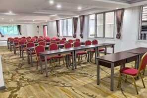 Een vergaderzaal met meerdere tafels en stoelen, grote ramen en een vloerbedekking.