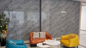 A modern lobby with a marble wall, a blue armchair, an orange sofa with patterned cushions, a yellow armchair, and a small round table with cups. - New Beacon Shennongjia Villa (Shennongjia)