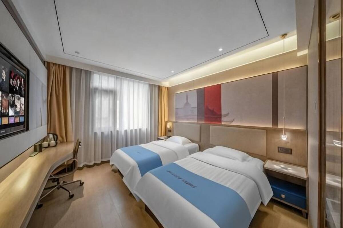 A hotel room with two beds, a desk, a TV, and a large window with curtains.