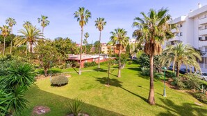 A well-maintained garden with palm trees and manicured lawns, surrounded by modern buildings.