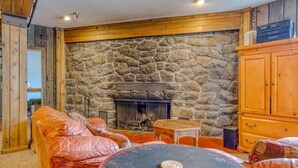 A cozy living room with a stone fireplace, leather sofas, and a small table. - Thunderhead Condo With Heated Pool & Mountain View (Government Camp)