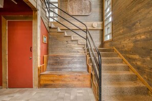 Una escalera con escalones de madera y barandillas metálicas, que lleva a una puerta roja.