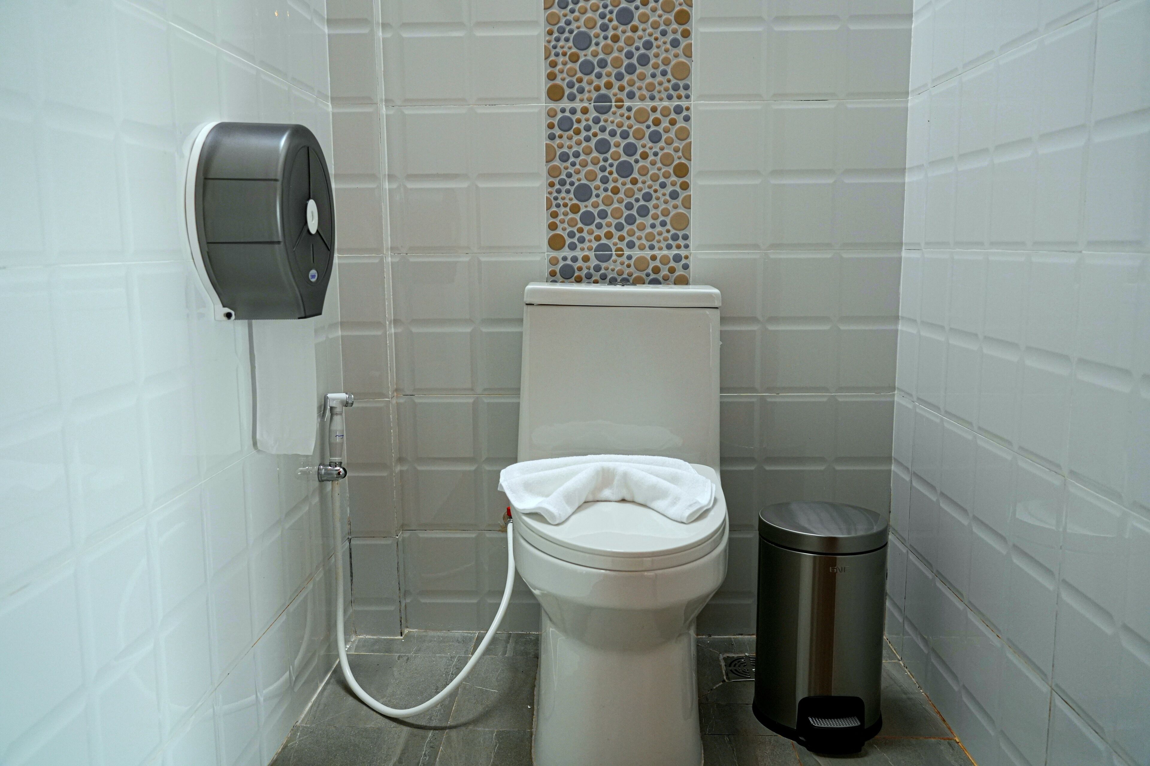 A small, modern bathroom with a toilet, a hand dryer, and a trash bin.