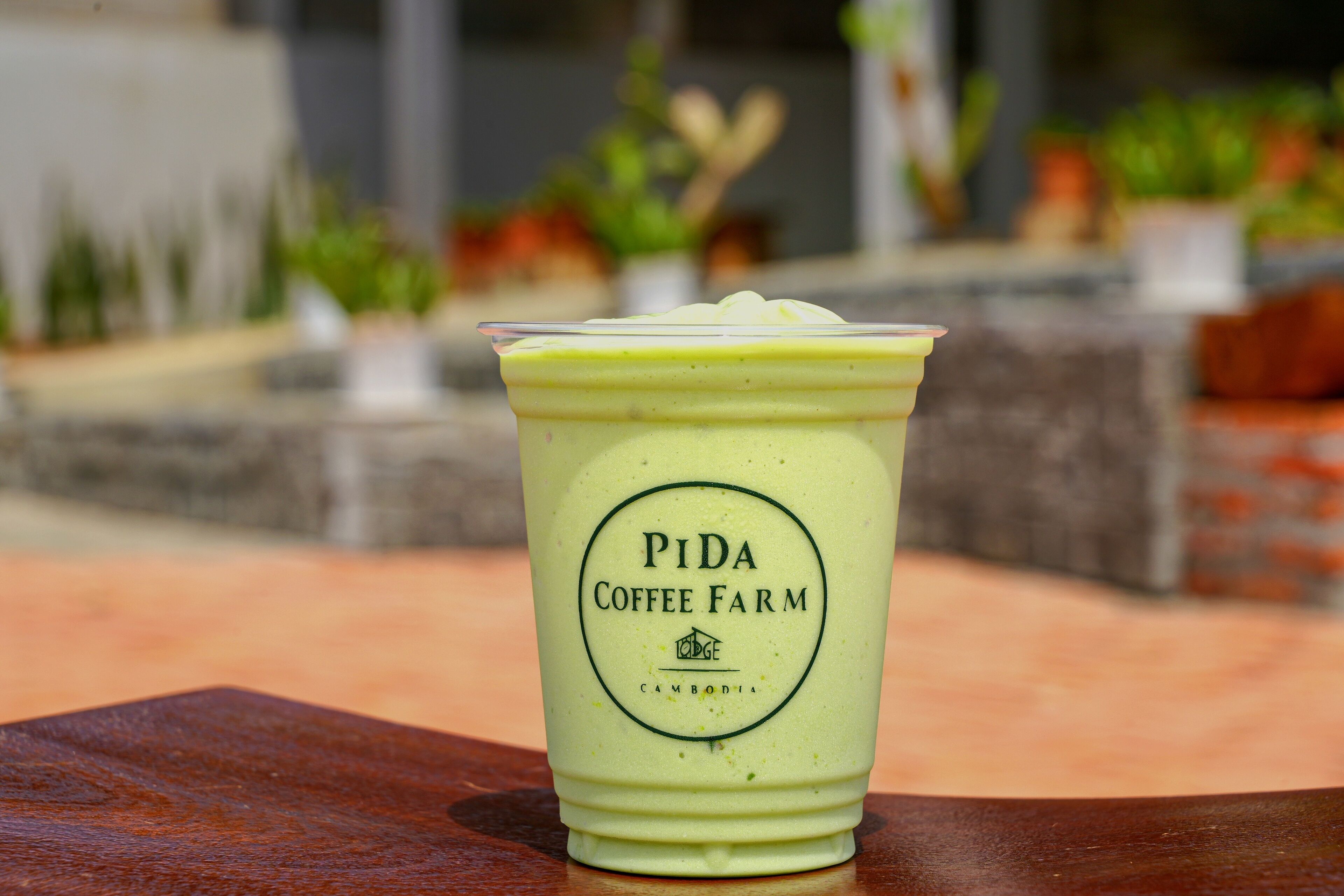 A Pida Coffee Farm cup with a green beverage on a wooden table.