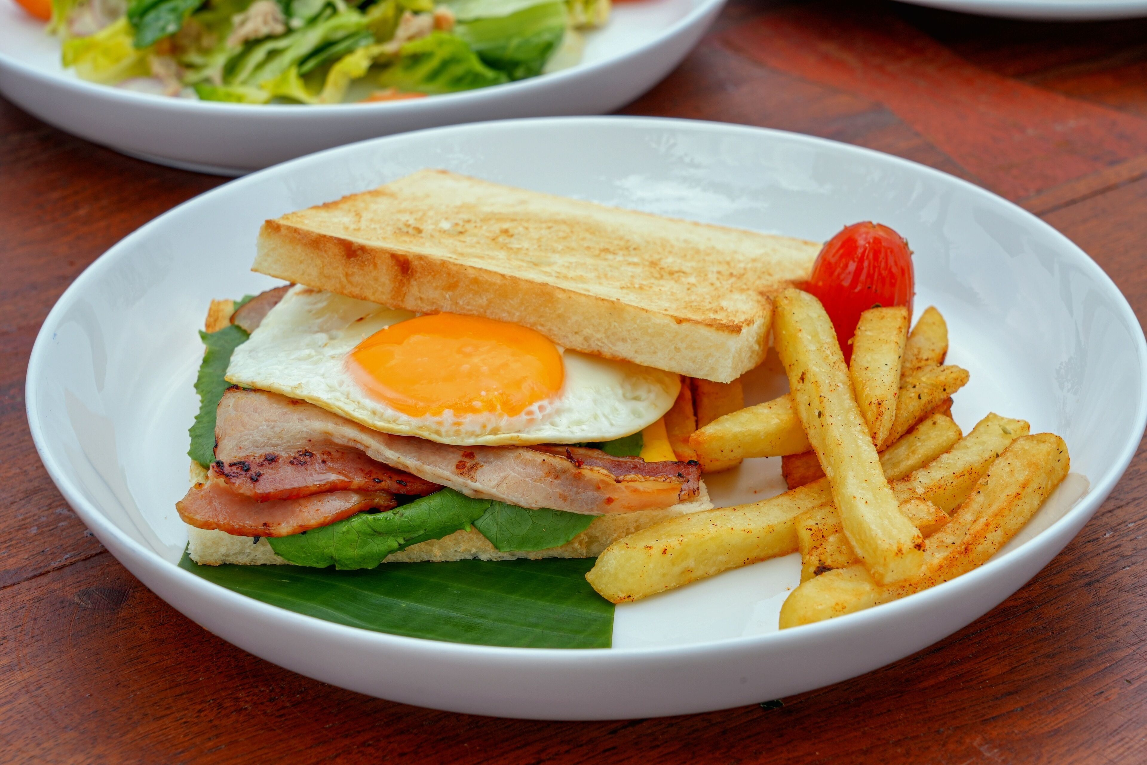 Un plato con un sándwich, huevo, tocino, lechuga y papas fritas.