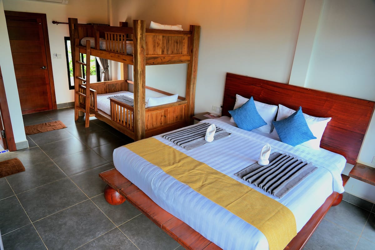Quarto com uma cama de solteiro, uma cama grande com cabeceira de madeira e uma mesinha de cabeceira.