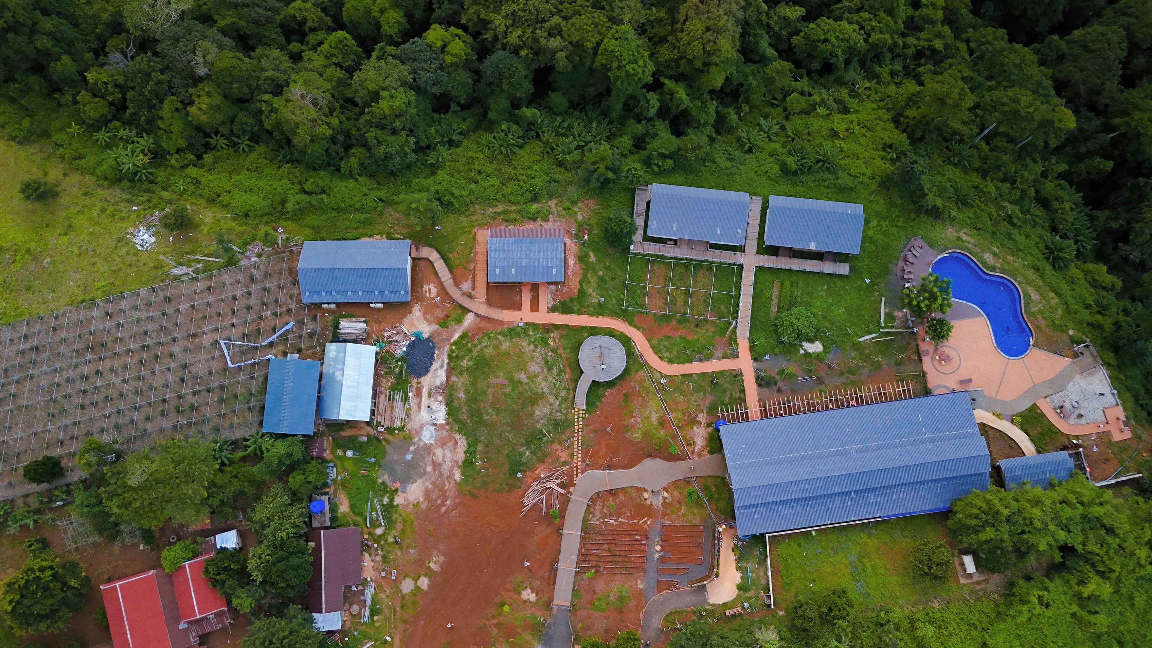 Vista aérea de una propiedad con varias edificaciones, una piscina y vegetación circundante.