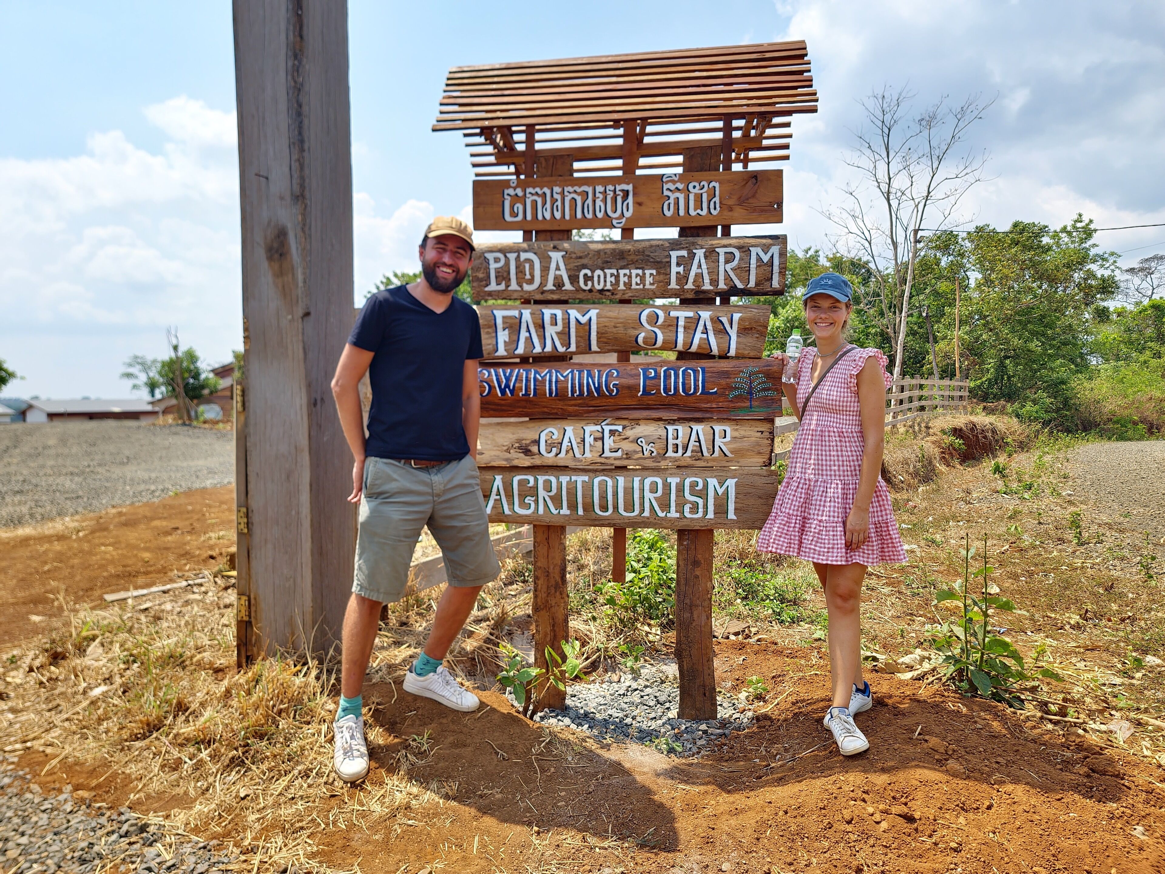 A wooden sign with text indicating a farm stay, coffee farm, swimming pool, cafe, bar, and agritourism.