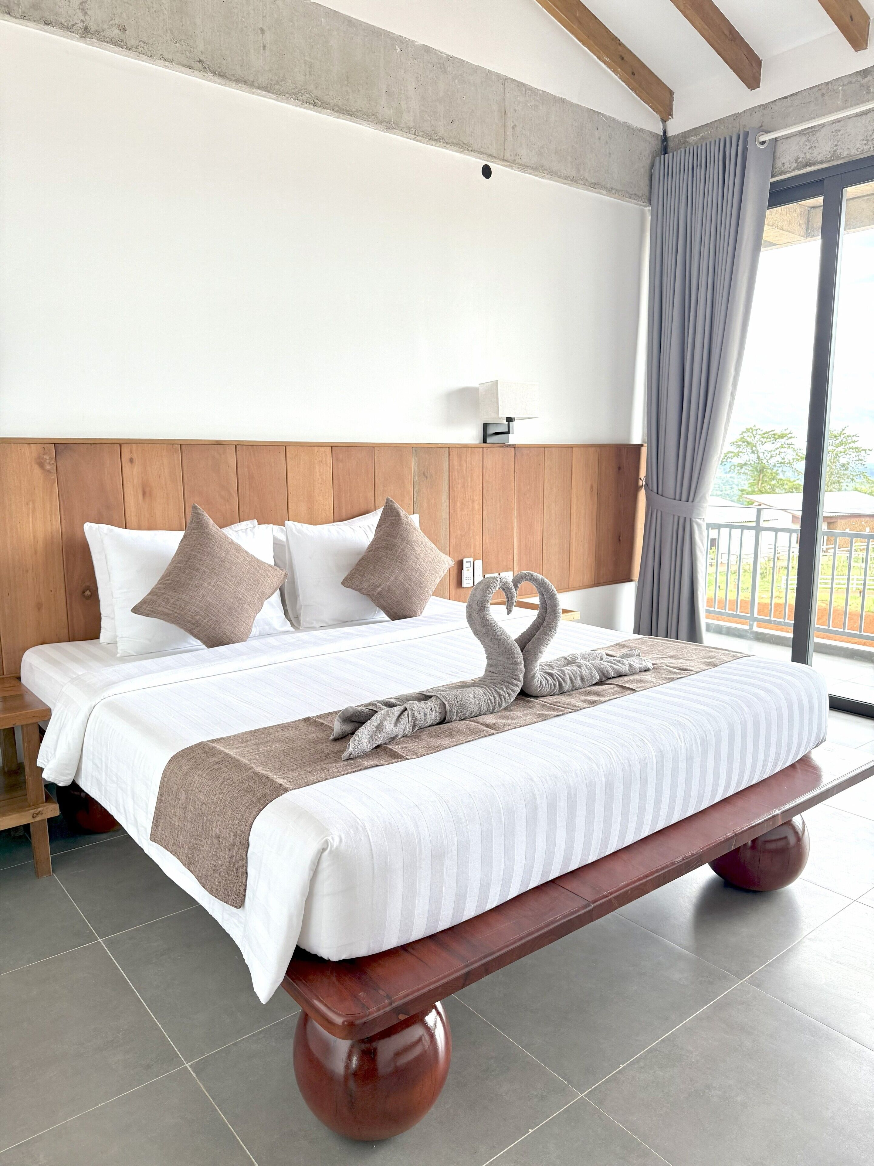 A hotel room with a bed, wooden headboard, and a view of the outdoors.